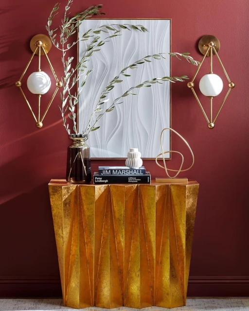 Interior space features a golden console table with a vase, books, abstract sculpture, and two sconces against a dark red wall.