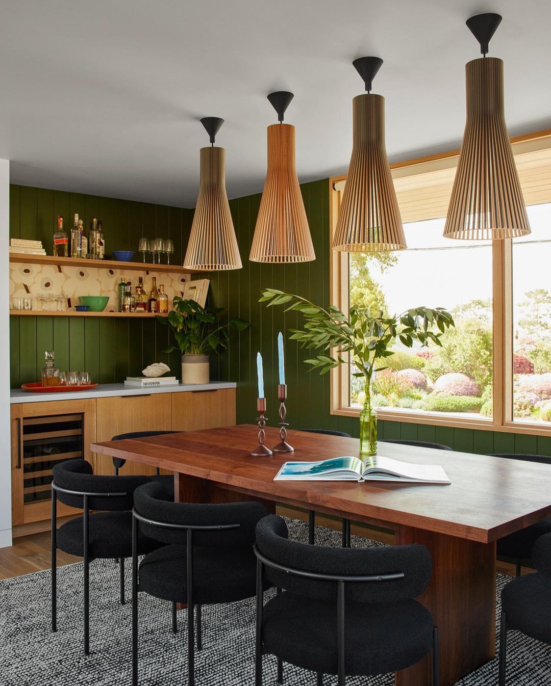 Modern dining room with wood table, black chairs, and unique pendant lights against dark green walls, creating an inviting, stylish space.