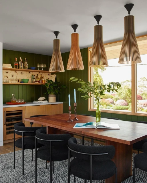 Modern dining room with wood table, black chairs, and unique pendant lights against dark green walls, creating an inviting, stylish space.