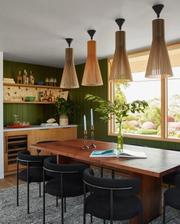 Modern dining room with wood table, black chairs, and unique pendant lights against dark green walls, creating an inviting, stylish space.