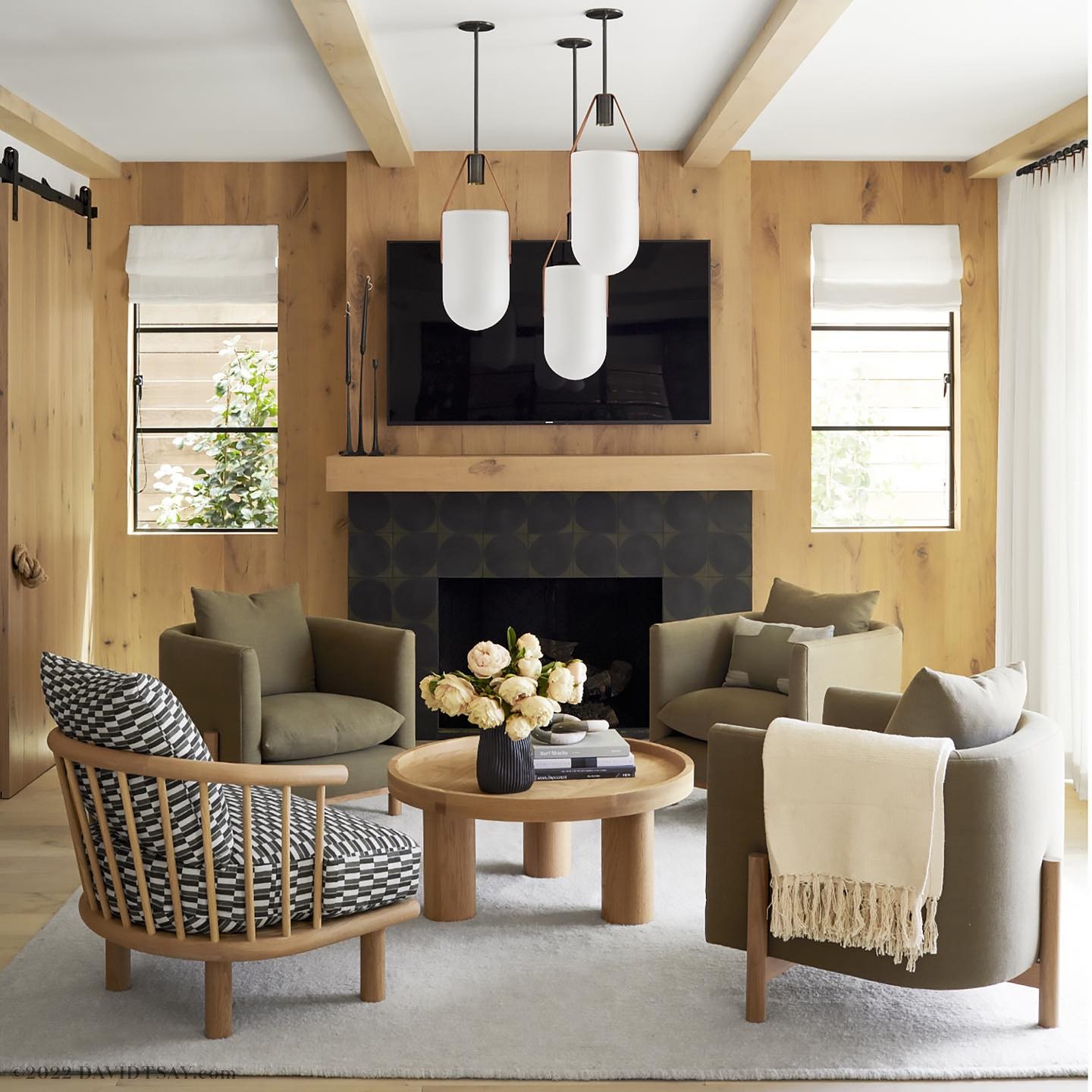 Living room interior featuring four armchairs around a round coffee table, with a fireplace, television, and modern pendant lights.