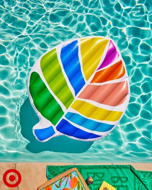 Top-down view of colorful inflatable leaf pool float in blue water, next to towel and Target logo on concrete pool edge.