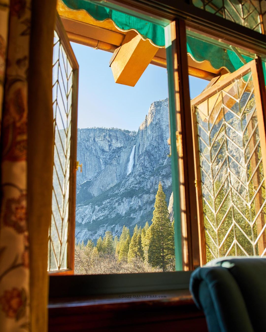 Scenic view of Yosemite waterfall and mountains seen through a window with decorative curtains and panes, showcasing the natural landscape.
