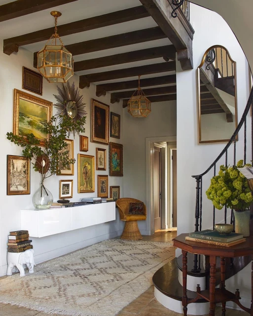 Entryway with vintage-style decor: gallery wall, wicker chair, stacked books on the floor, ornate light fixtures, and patterned rug.