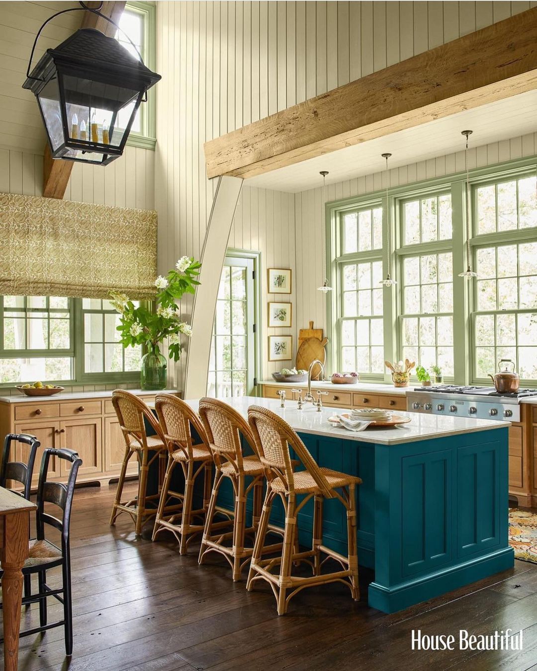 Bright kitchen with a turquoise island, wicker bar stools, light wood cabinets, light green trim, and dark wood floors in a home interior.