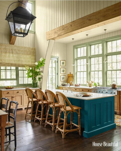 Bright kitchen with a turquoise island, wicker bar stools, light wood cabinets, light green trim, and dark wood floors in a home interior.
