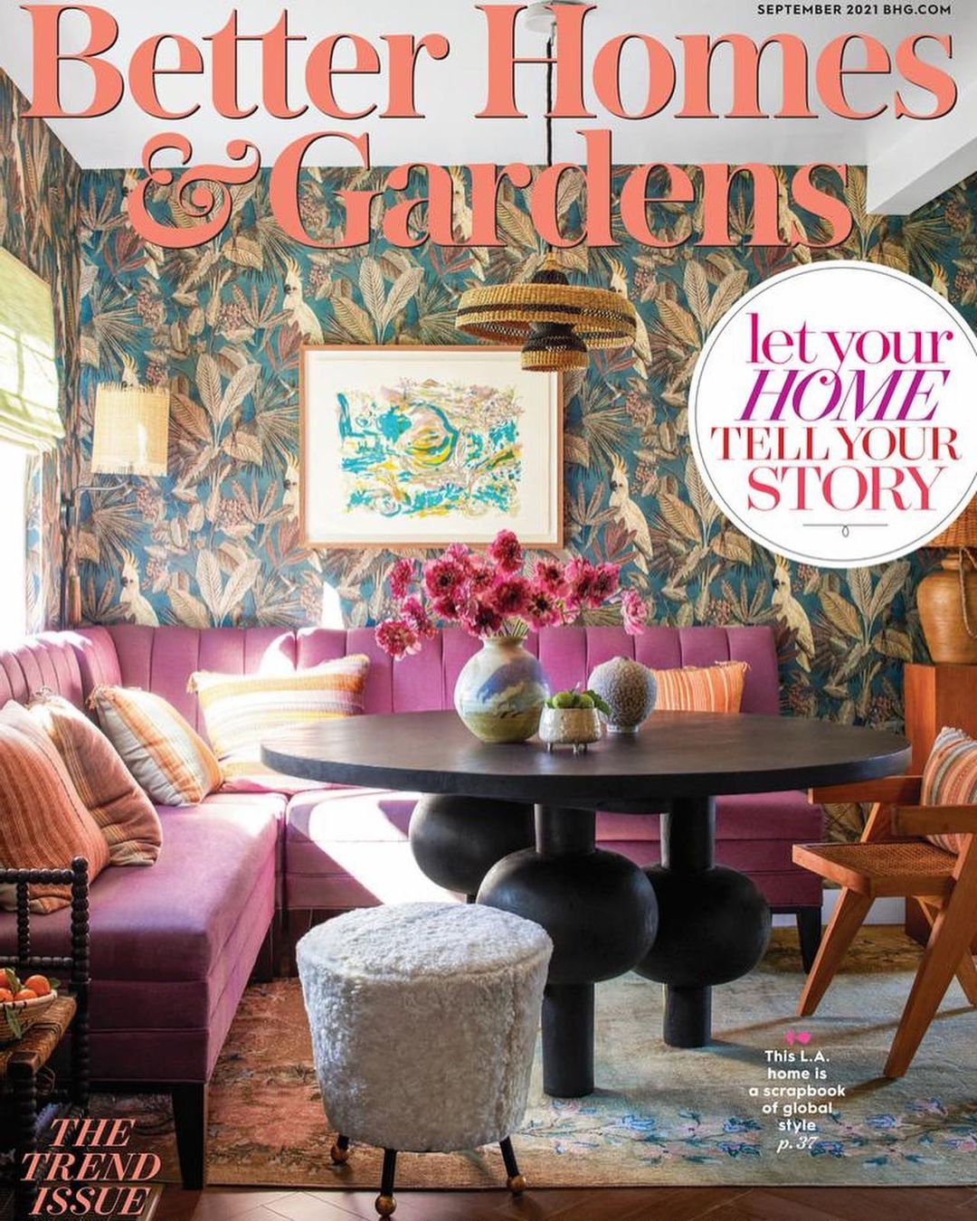 Interior design featuring a round table with floral centerpiece, purple sectional sofa, and botanical wallpaper in a home setting.