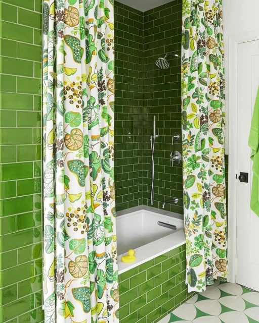 Bathroom interior with green tile walls, floral shower curtain, white bathtub, and round-patterned floor tile. Bathtub has a yellow duck.