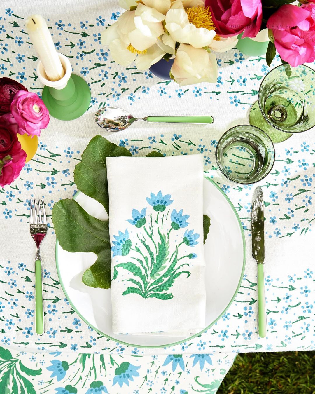 Overhead shot of a table setting with a floral-patterned tablecloth, plate, floral-printed napkin, silverware, glassware, and flowers.