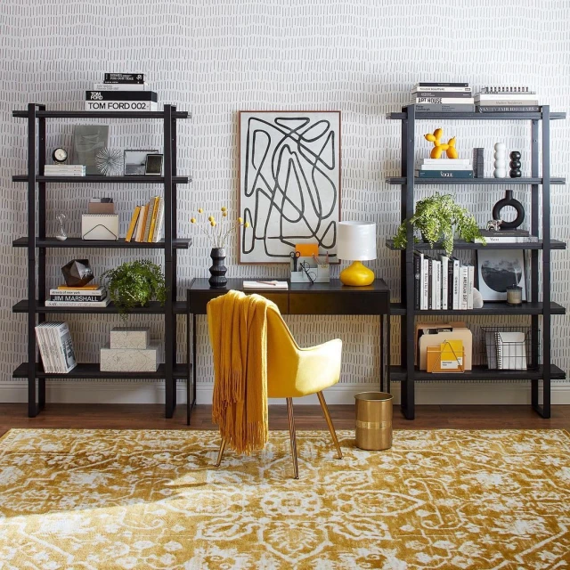 Interior shot of a home office featuring a black desk, yellow chair, and bookshelves filled with books and decorative objects.
