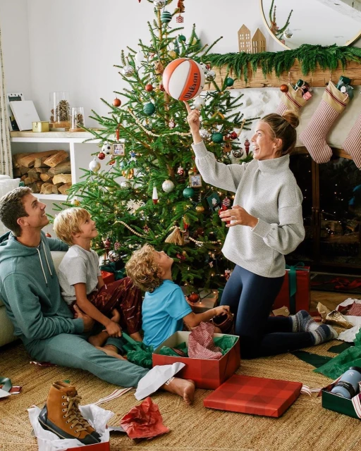 Family of five opening presents around a Christmas tree indoors. A woman balances a basketball on her finger.