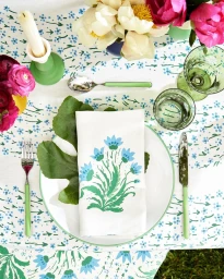 Overhead view of a beautifully set dining table with a floral patterned tablecloth, white plate, green napkin, cutlery, and fresh flowers.