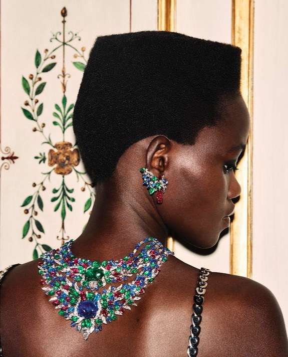 Profile view of an adult woman with jewelry. The woman has dark skin, short black hair, and wears large jeweled earrings and necklace.