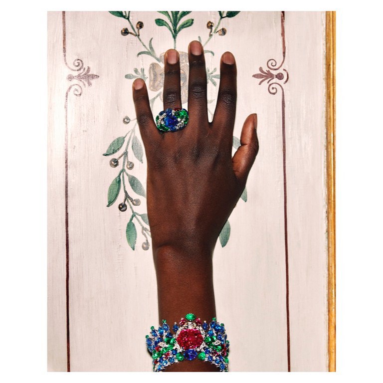Close-up of a dark-skinned human arm adorned with a ring and a bracelet. The jewelry features intricate designs with red, blue, and green stones.