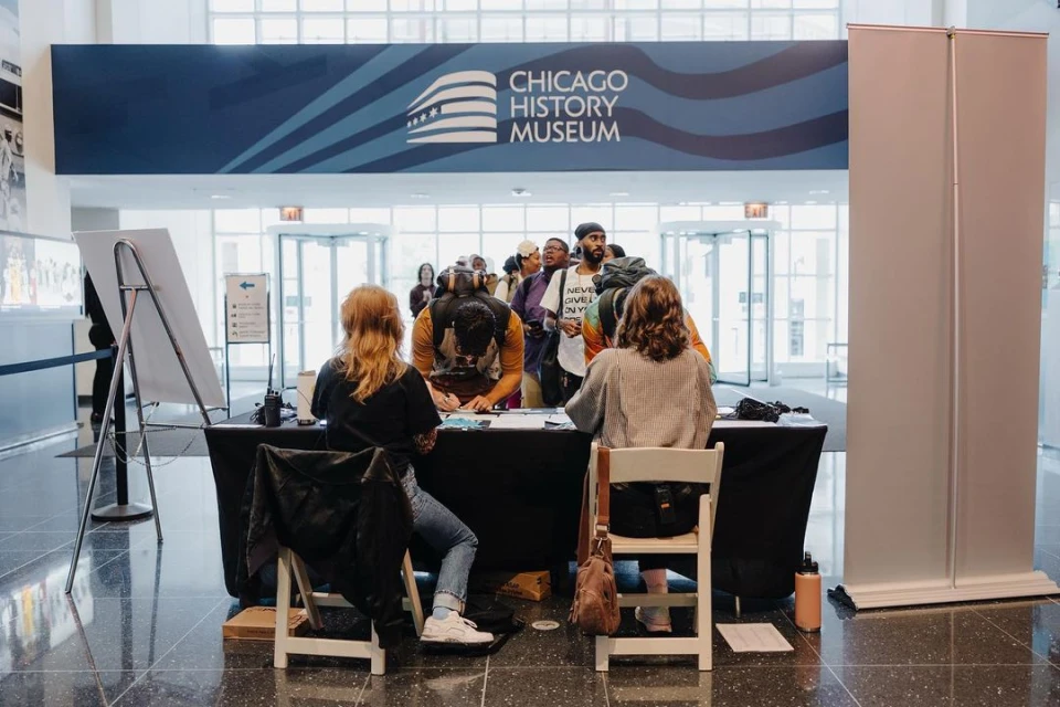 Visitors line up at a registration table inside the Chicago History Museum, with a large sign visible in the background.