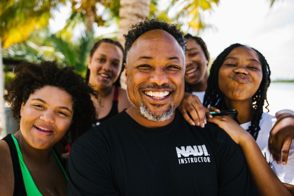 Smiling man poses with four smiling young women on a sunny day near palm trees, showcasing a happy and candid moment.