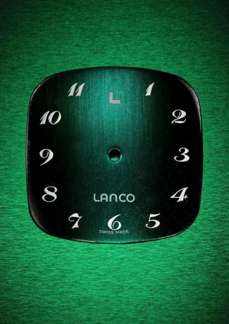 Close-up of a vintage LANCO watch face with black and turquoise coloring and white numerals on a green, textured surface.