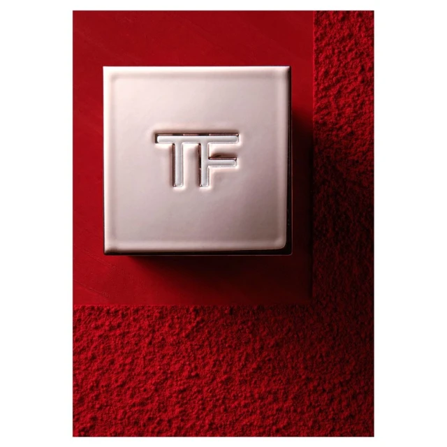 Close-up product shot of a rose gold makeup compact with the TF logo on a red, textured surface. Beauty product photography.