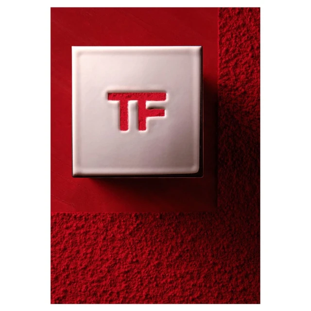 Tom Ford cosmetic product in square silver packaging with the TF logo in red, resting on a textured red surface. Beauty aesthetic.