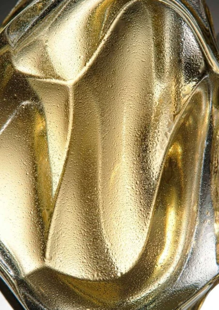 Abstract macro photograph of an ornamental gold glass vase with textured patterns and water droplets on its surface, casting soft shadows.