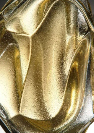 Abstract macro photograph of an ornamental gold glass vase with textured patterns and water droplets on its surface, casting soft shadows.
