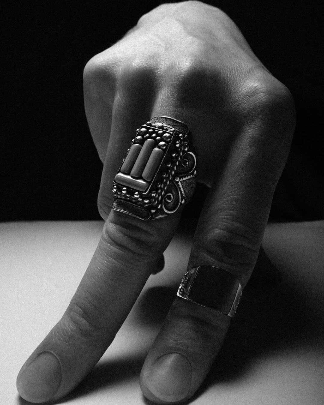 Close-up shot showcasing an adult human hand wearing ornate silver rings, set against a blurred dark background.
