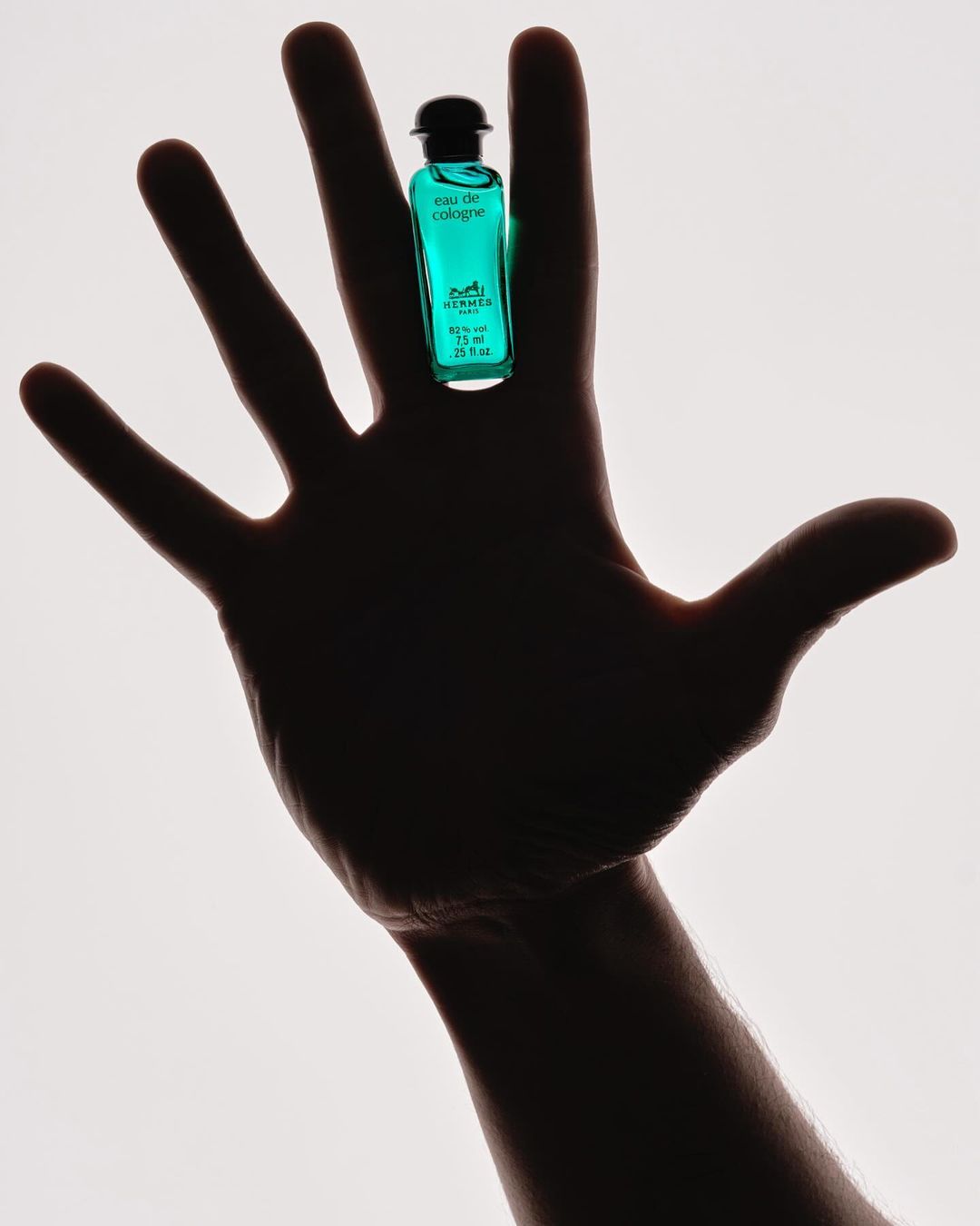 Cologne bottle held on outstretched hand against a white background in a studio shot showcasing product and human element.