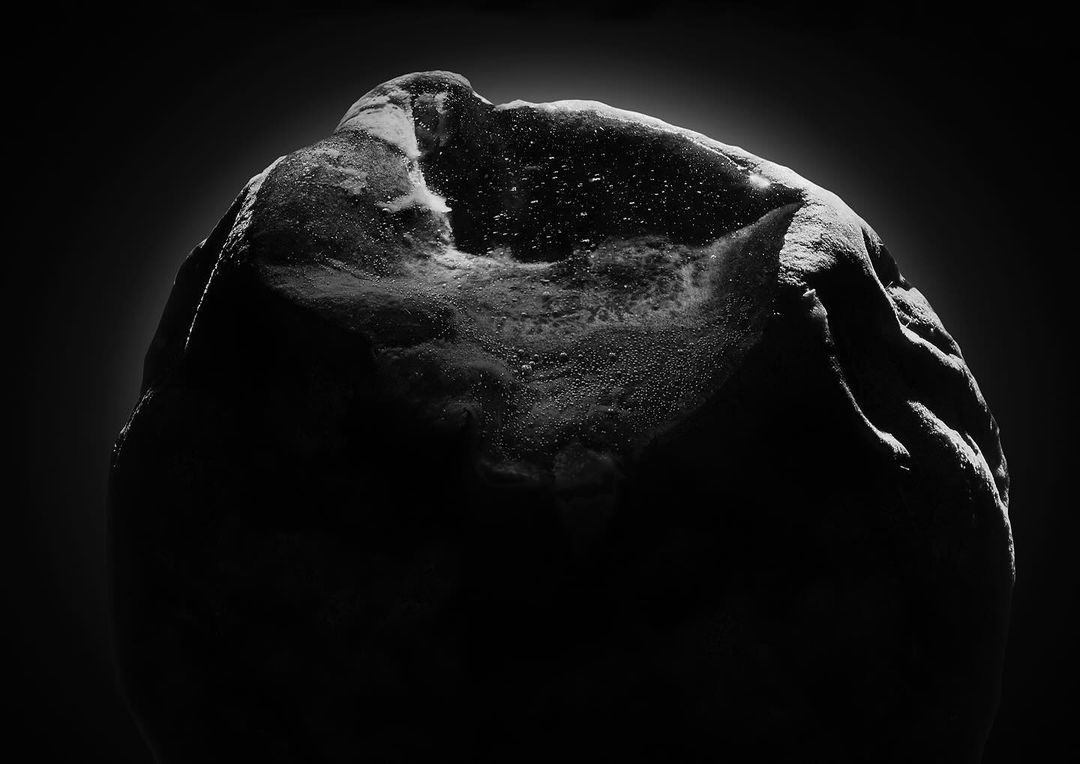 Monochromatic, high-contrast close-up photo of a rock illuminated against a dark background, showcasing its textures and droplets.