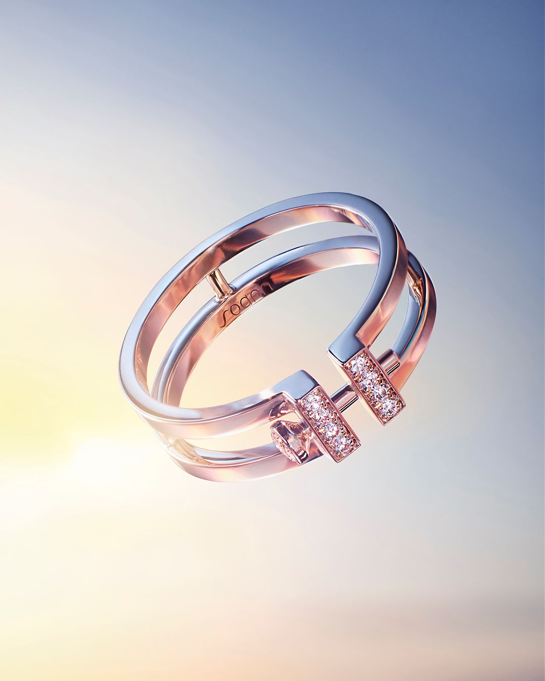 A metal ring with diamonds is displayed against a gradient background of yellow, white, and blue in a studio-lit product shot.