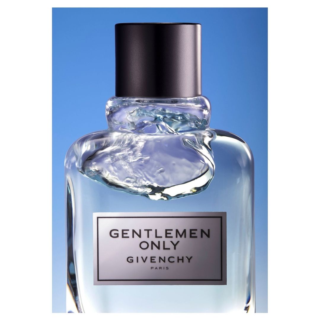 Close-up product shot of a glass perfume bottle with a black cap against a gradient blue background