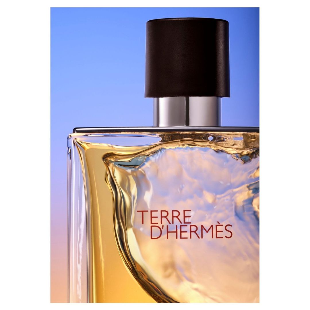 Close-up studio shot of a Terre d'Hermès fragrance bottle showcasing its golden liquid and sophisticated design against a blue background.