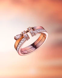 Rose gold ring with diamonds and a pear-shaped gemstone floating against a warm gradient background