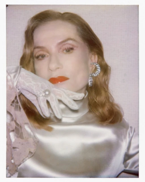 Portrait of a fair-skinned adult woman with red lipstick wearing a white lace glove, statement earrings, and a cream colored high neck top.