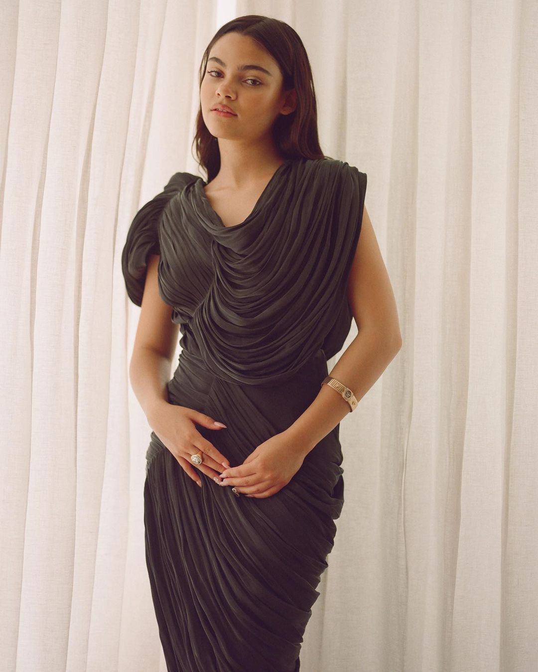 Woman in a dark pleated dress posing against white sheer curtains photographed by Davis Bates.