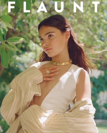 Ariana Greenblatt wearing a gold choker necklace and white top with a pinstripe jacket outdoors in a garden.