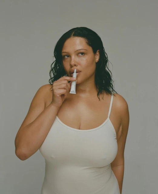 Woman applies lip cream in a studio setting with neutral background, showcasing beauty and personal care.