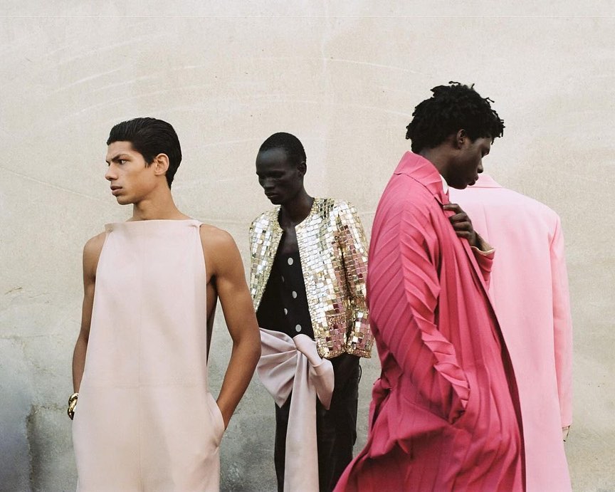 Fashion editorial shot featuring four men in stylish outfits against a neutral wall, showcasing modern menswear with unique designs.