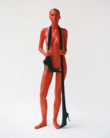 Adult female standing in a bright white photo studio, with high heel shoes suspended from her neck.