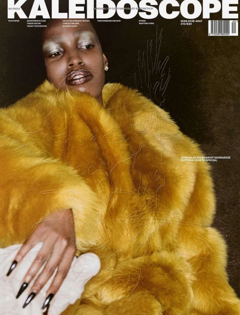 Magazine cover features a black woman in a yellow fur coat. Dramatic makeup, silver eyeshadow, and dark background. Editorial fashion shot.