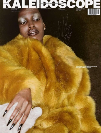 Magazine cover features a black woman in a yellow fur coat. Dramatic makeup, silver eyeshadow, and dark background. Editorial fashion shot.
