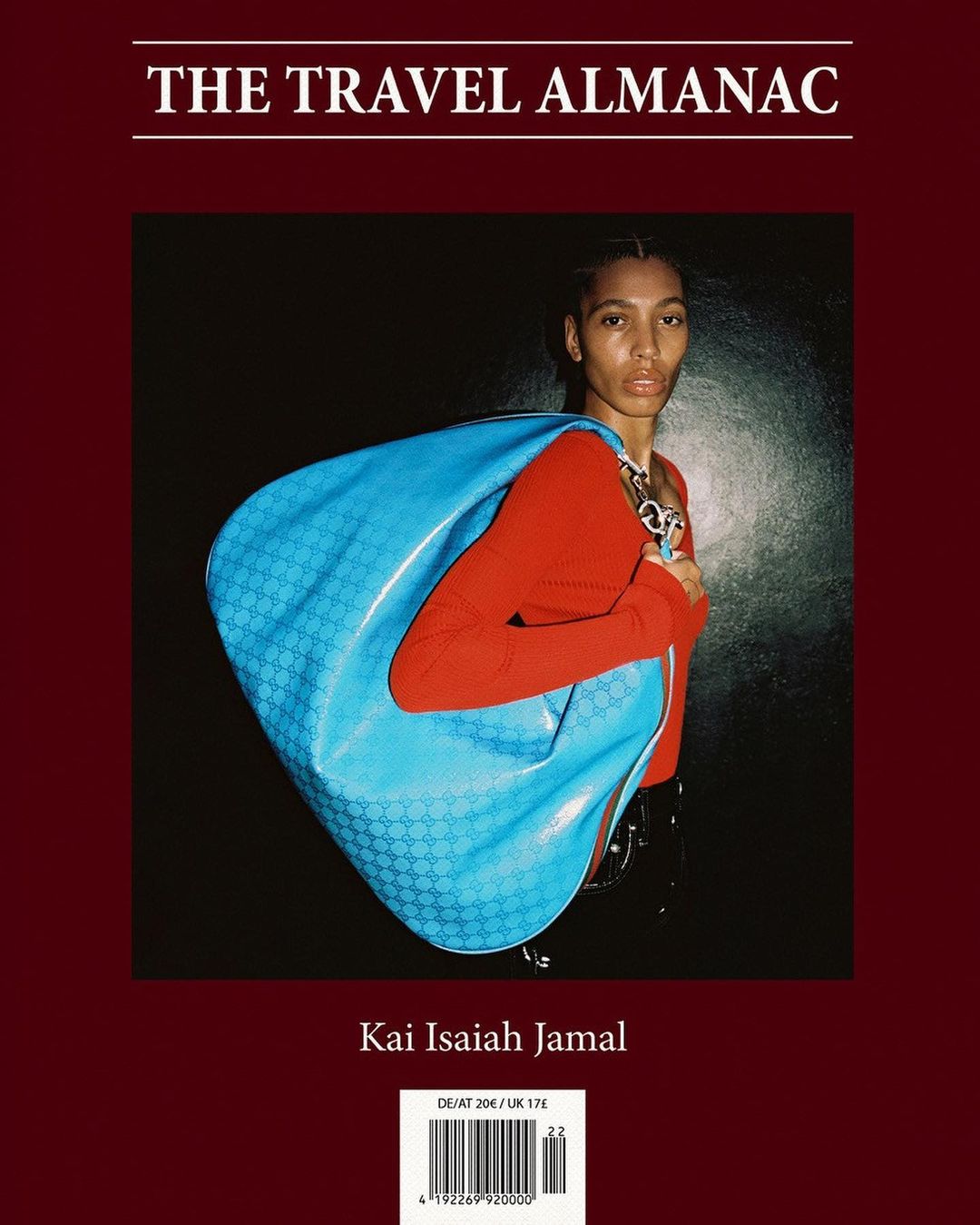 Magazine cover featuring a person in a red top with a large blue bag, against a dark background, promoting 'The Travel Almanac'.