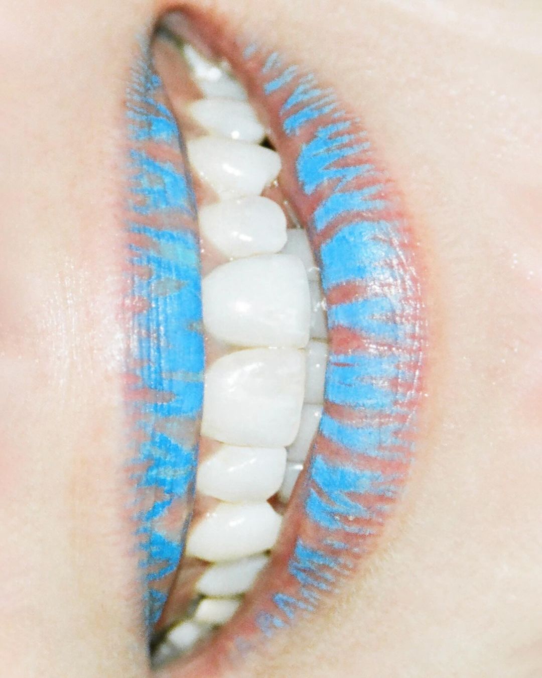 Close-up portrait of lips wearing textured blue lipstick with white teeth visible between them.