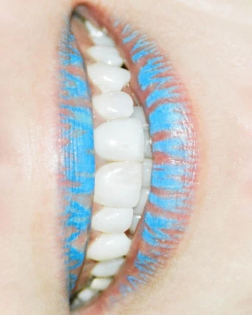 Close-up portrait of lips wearing textured blue lipstick with white teeth visible between them.