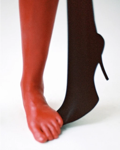 Close-up of one bare red foot with a black stocking and high-heeled shoe on the other foot against a white background.