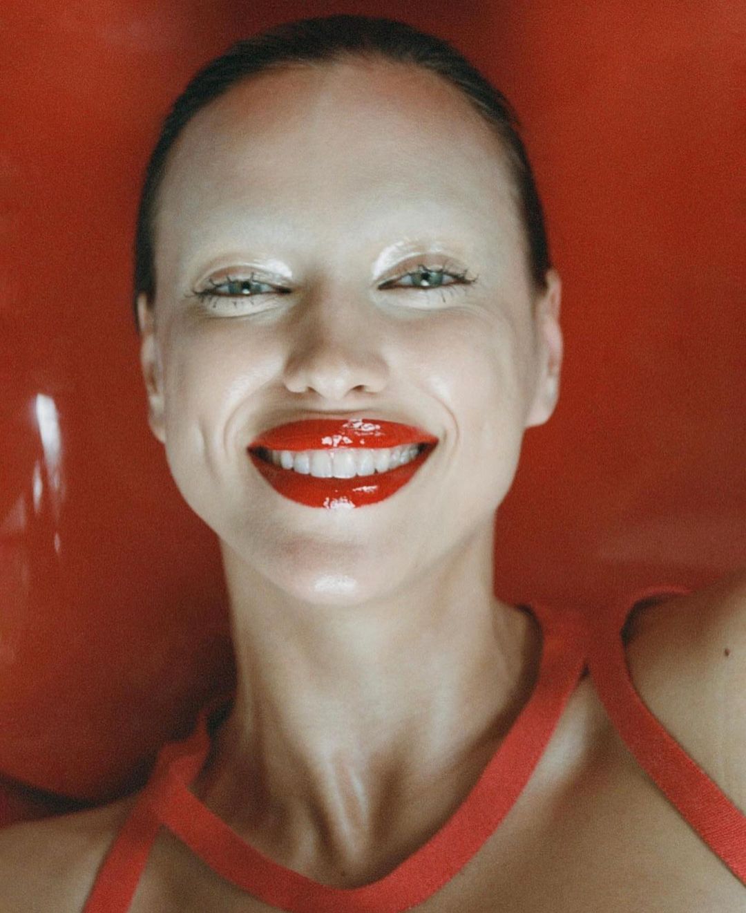 Close-up portrait of a woman with red lipstick and painted eyebrows against a vibrant red backdrop, fashion-forward and striking.