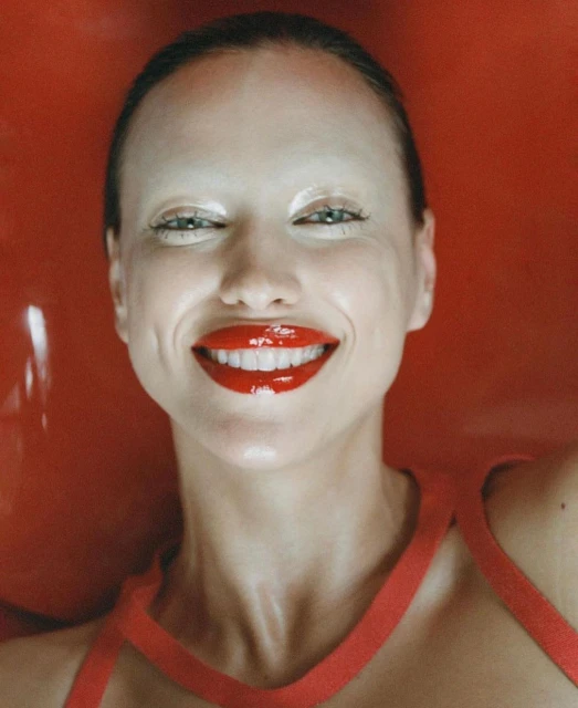Close-up portrait of a woman with red lipstick and painted eyebrows against a vibrant red backdrop, fashion-forward and striking.