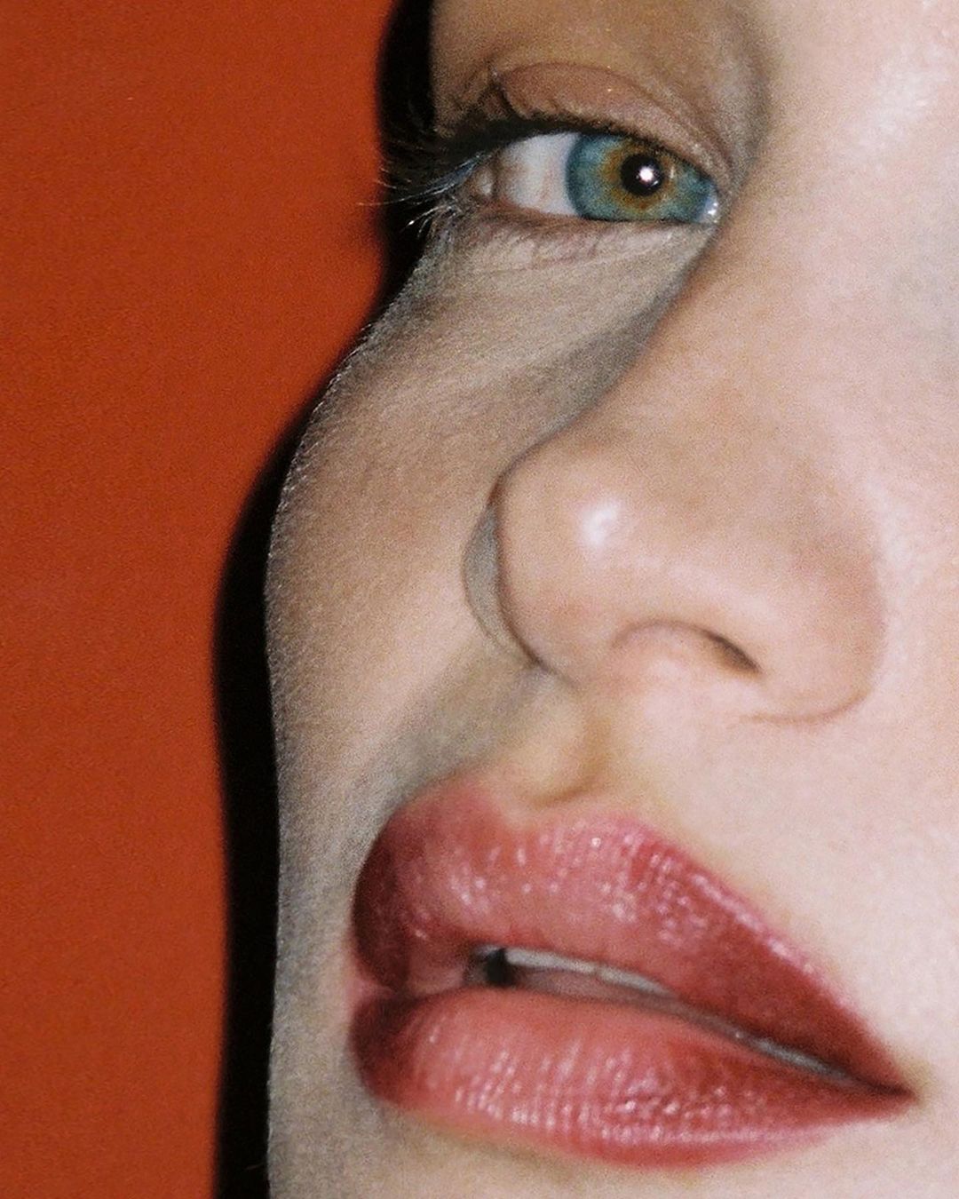 Extreme close-up portrait of a woman's face highlighting her blue eye and lips against a warm orange background.