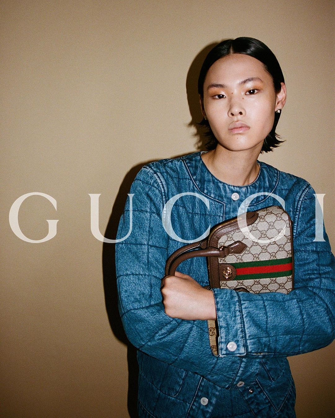 Model in quilted denim jacket holding monogram handbag by Davit Giorgadze