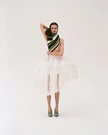 Model wearing a striped scarf and structured white fringed skirt standing against a white seamless background
