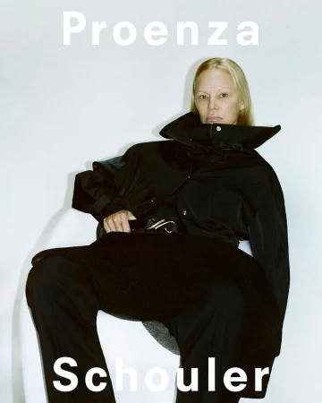 Model wearing a black jacket and dark trousers seated against a plain white background with bold white typography.